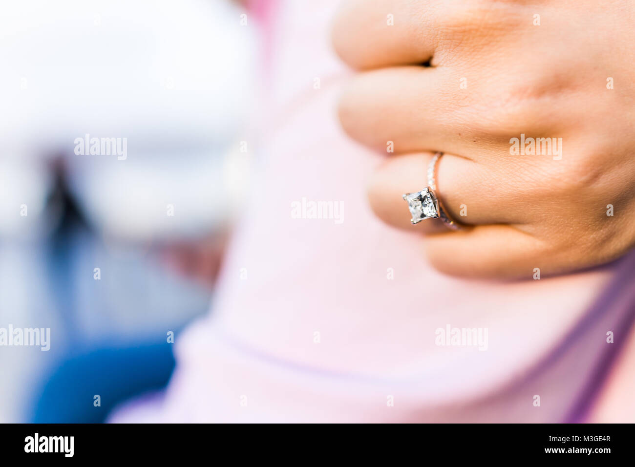 Young woman's hand with diamond engagement ring princess cut, gold outside outdoors on fiance man arm pink shirt love fist Stock Photo