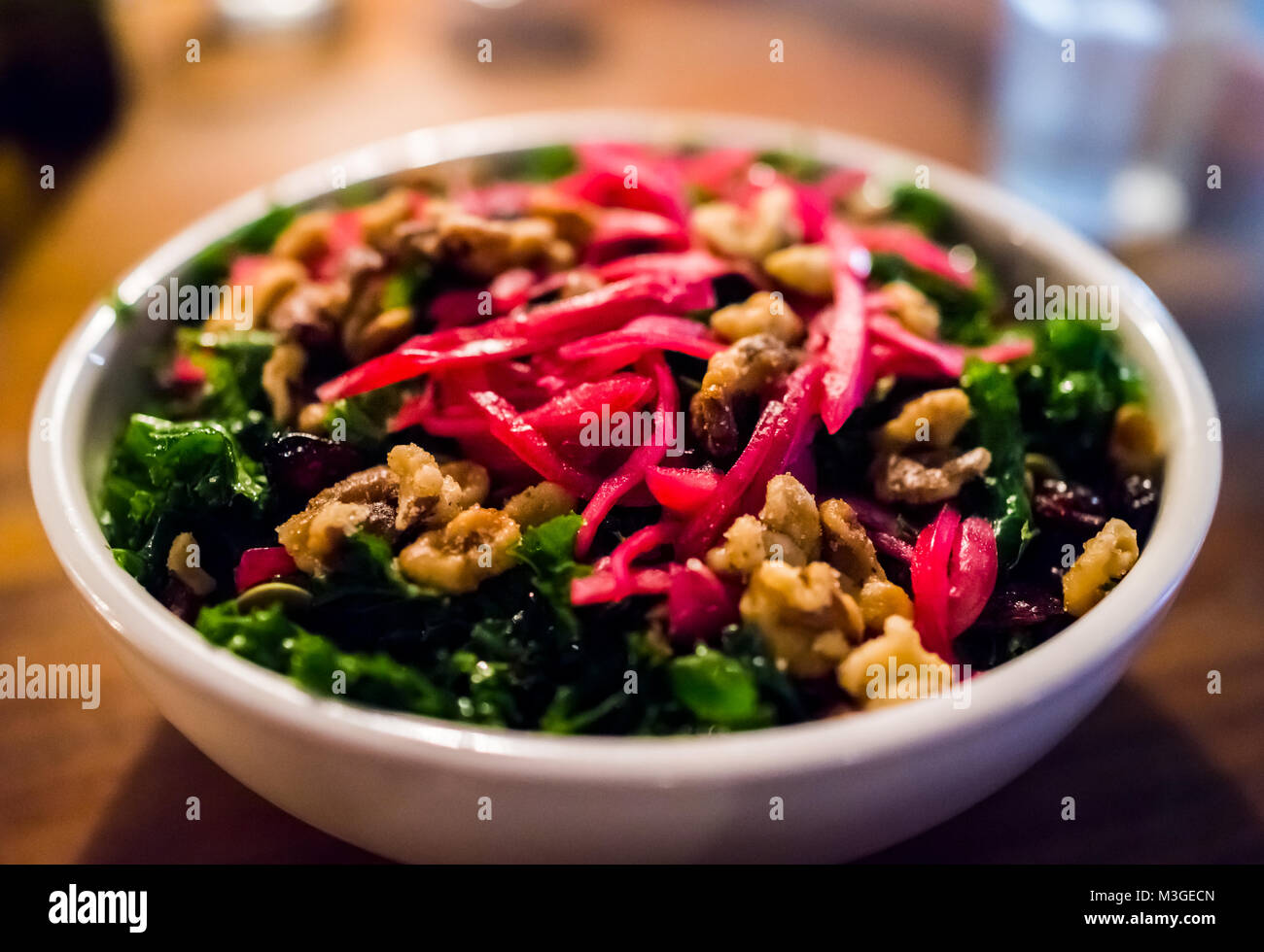 Macro closeup of kale red pepper beet shredded green vegan vegetarian salad in restaurant with candied nuts, walnuts, on wooden table in evening dinne Stock Photo