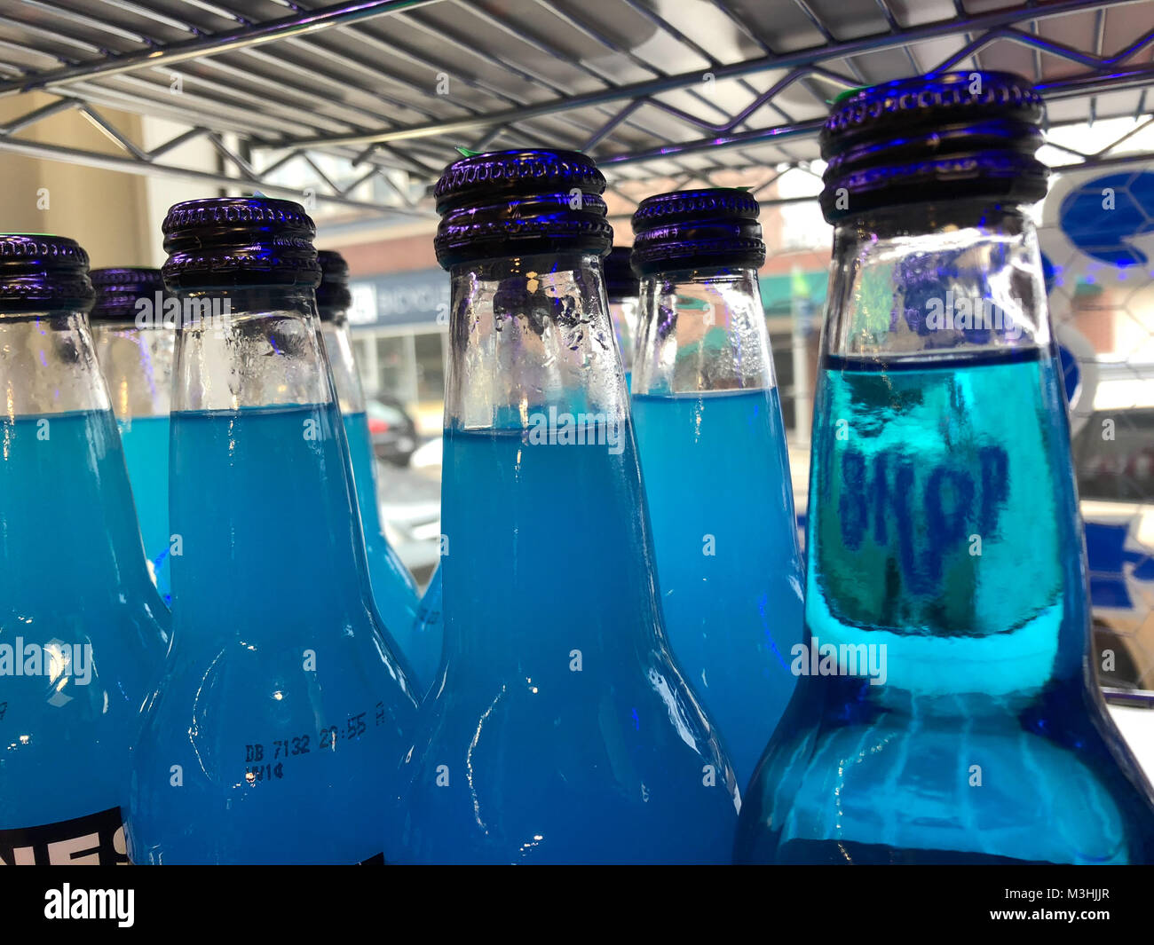 several blue soda drinks in bottles on a shelf with the reflection of the word shop in one bottle Stock Photo