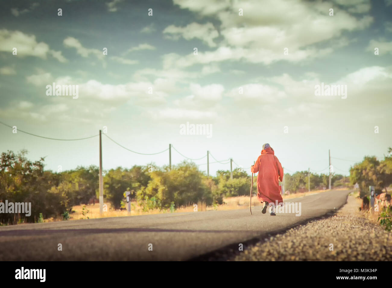 Goat keeper shepherd walking cane lonely road orange djellaba Stock Photo