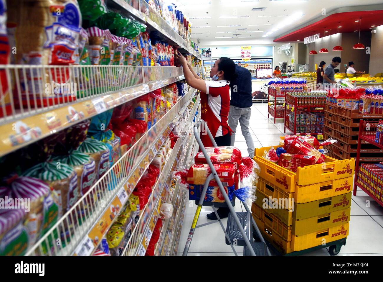 TAYTAY, RIZAL, PHILIPPINES - JANUARY 29, 2018: A worker arranges different kinds of bread on a display rack inside a grocery store. Stock Photo