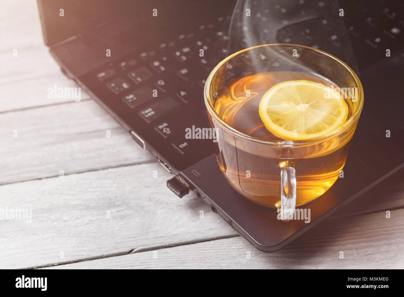 cup of tea with lemon on laptop and white wooden background, concept of tea time, relax with copy space. Stock Photo