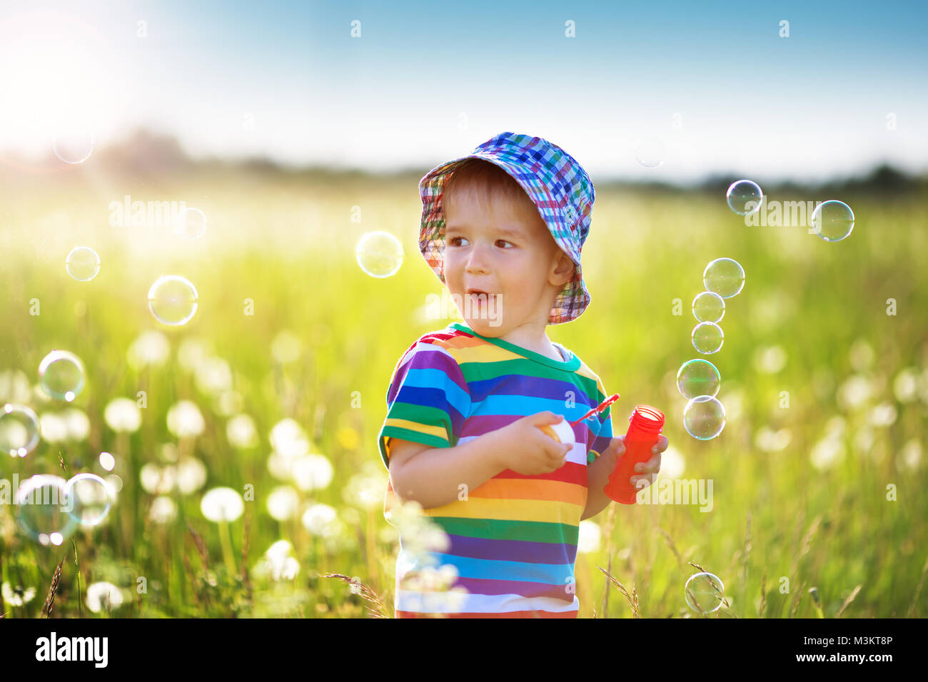 Baby boy standing in grass on the fieald with dandelions Stock Photo