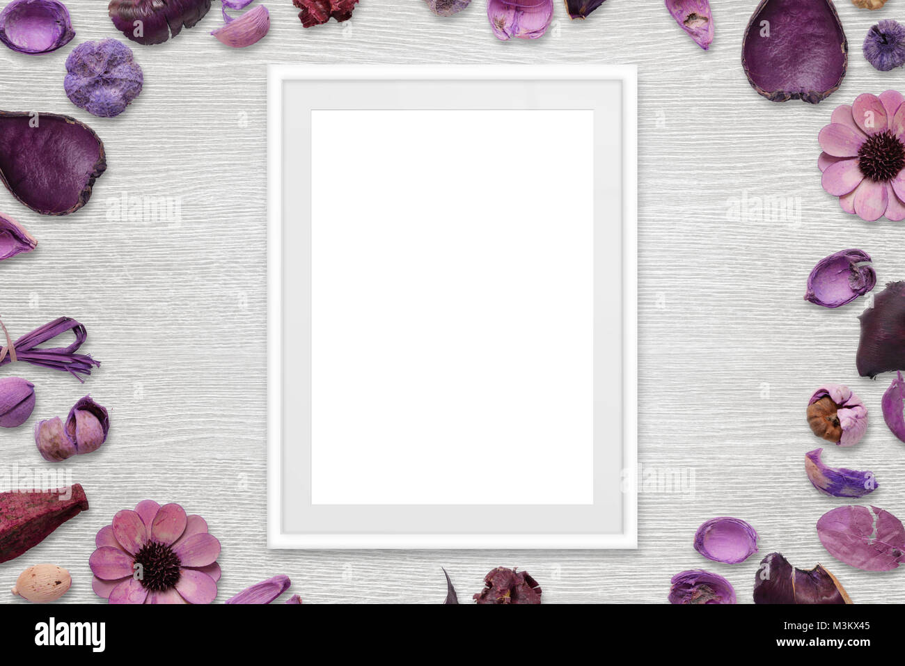 Picture frame with isolated white space for picture or text. Flower decorations around the frame. White wooden desk in background. Top view. Stock Photo