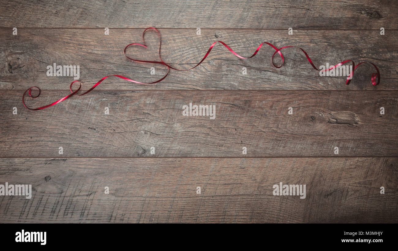 The red ribbon is lined in the shape heart on a dark wooden table ...
