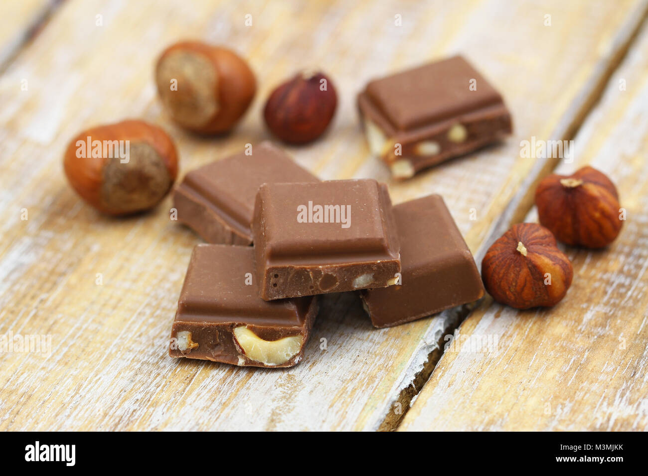 Few pieces of milk chocolates with hazelnuts on rustic wooden surface Stock Photo