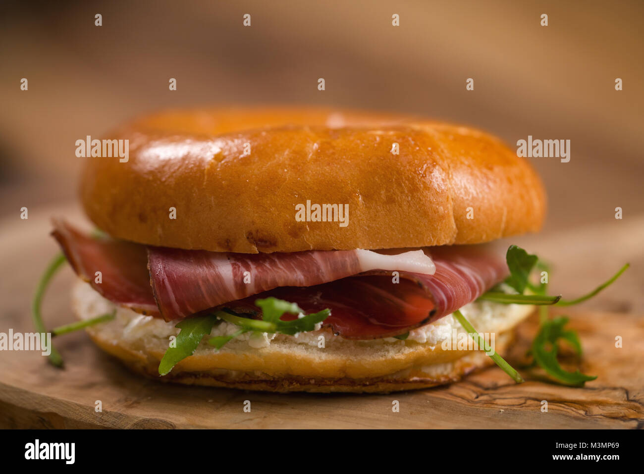 bagel sandwich with prosciutto and cream cheese on wood board Stock