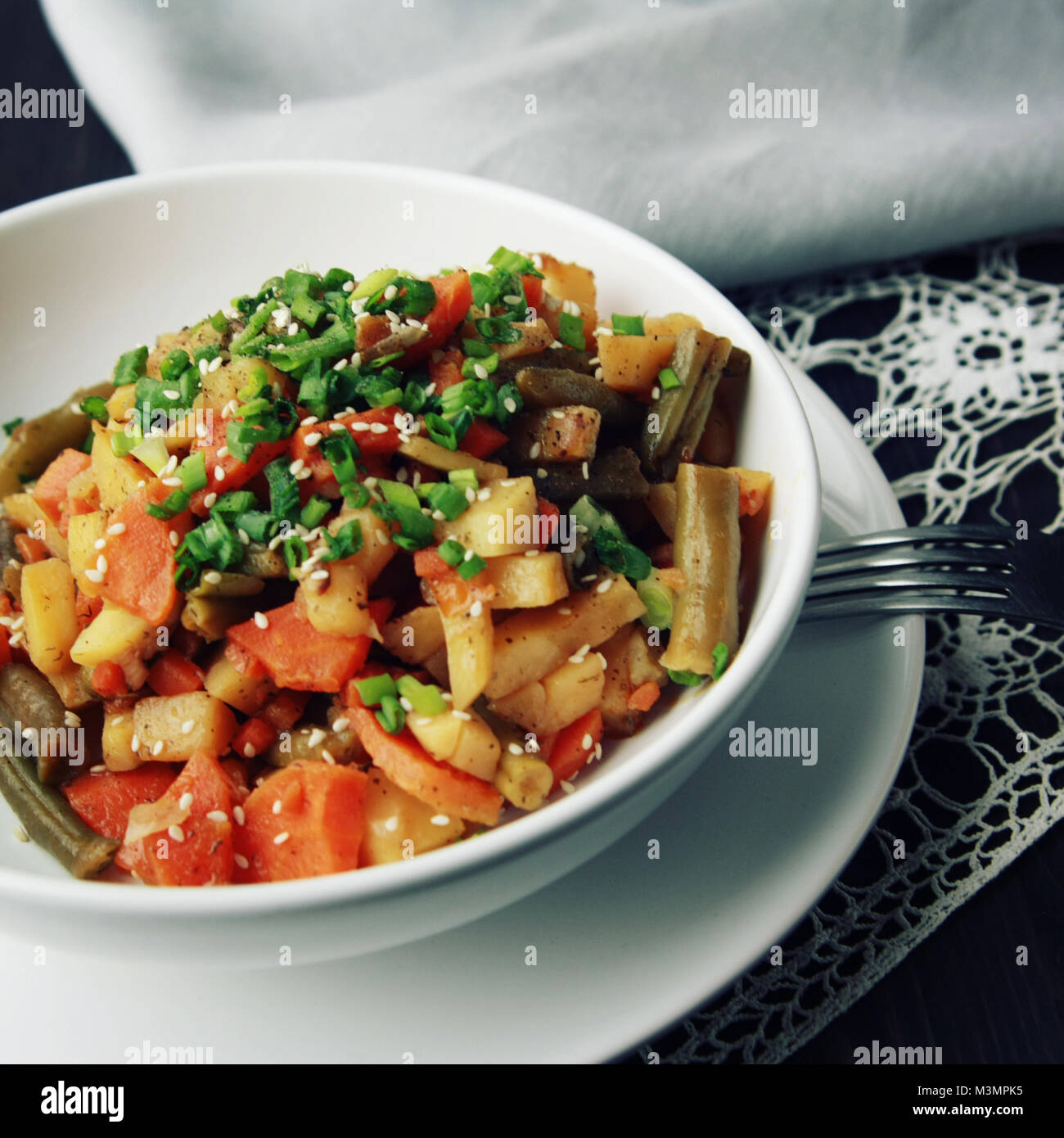 Vegan stew on the round white plate. Vegetarian dish with potato, carrot and green beans. Topped with chives and black pepper. European cuisine. Color Stock Photo