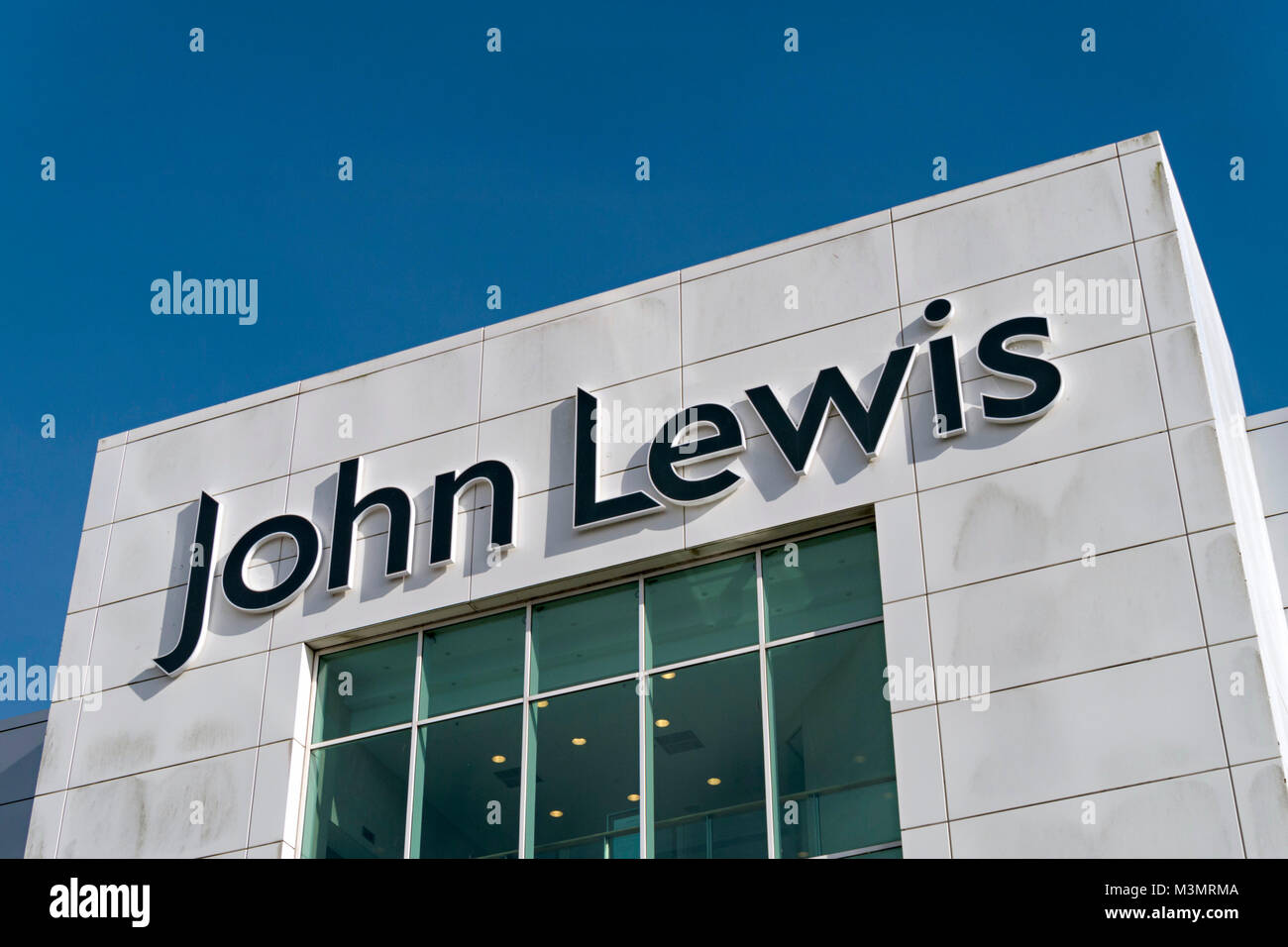 Large black John Lewis shop trademark logo on sunlit white exterior wall with blue sky above The Mall at Cribbs Causeway, Bristol, England, UK Stock Photo