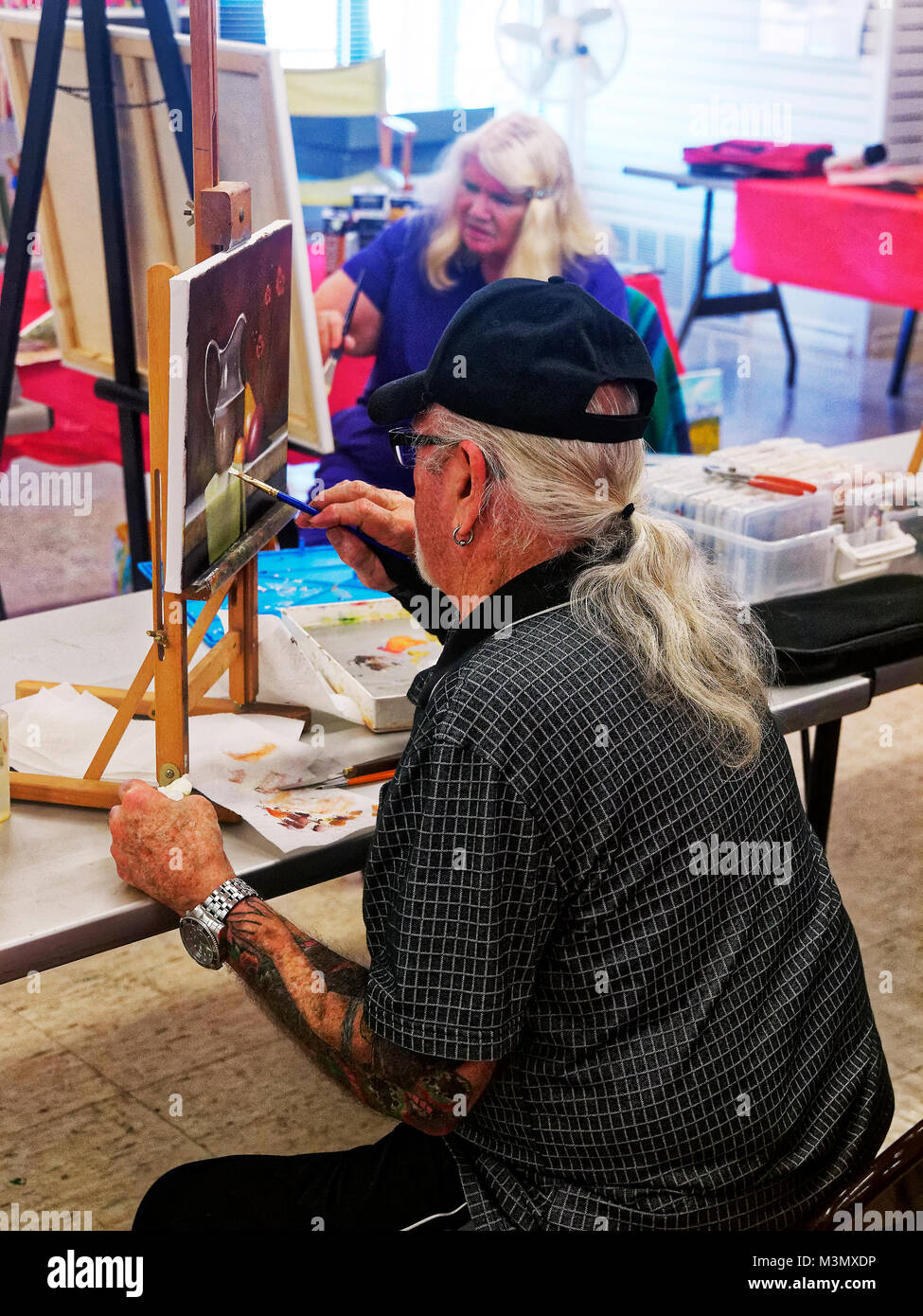 Seniors having lived a long hard life still stay active expressing themselves in painting class, and instructor Mahto Hogue with brace on wrist instructs by working on one of their paintings Stock Photo