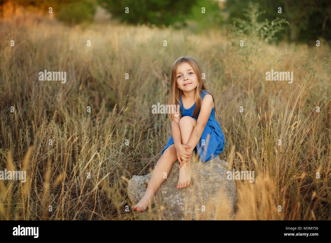 A little girl in a blue dress is sitting on the stones in the middle of ...