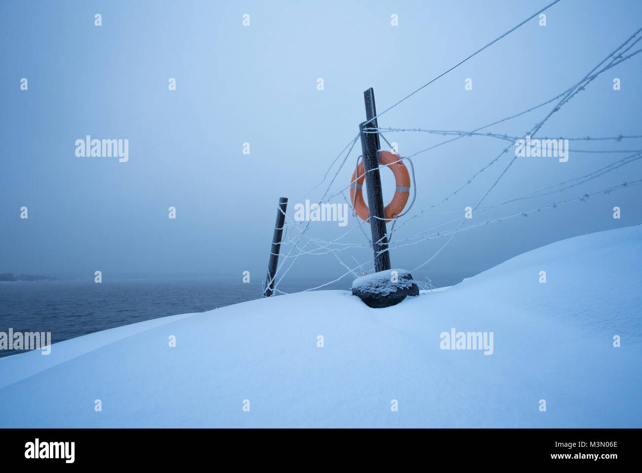 Simplistic view of barbed wire fence with life buoy against foggy sea at winter Stock Photo