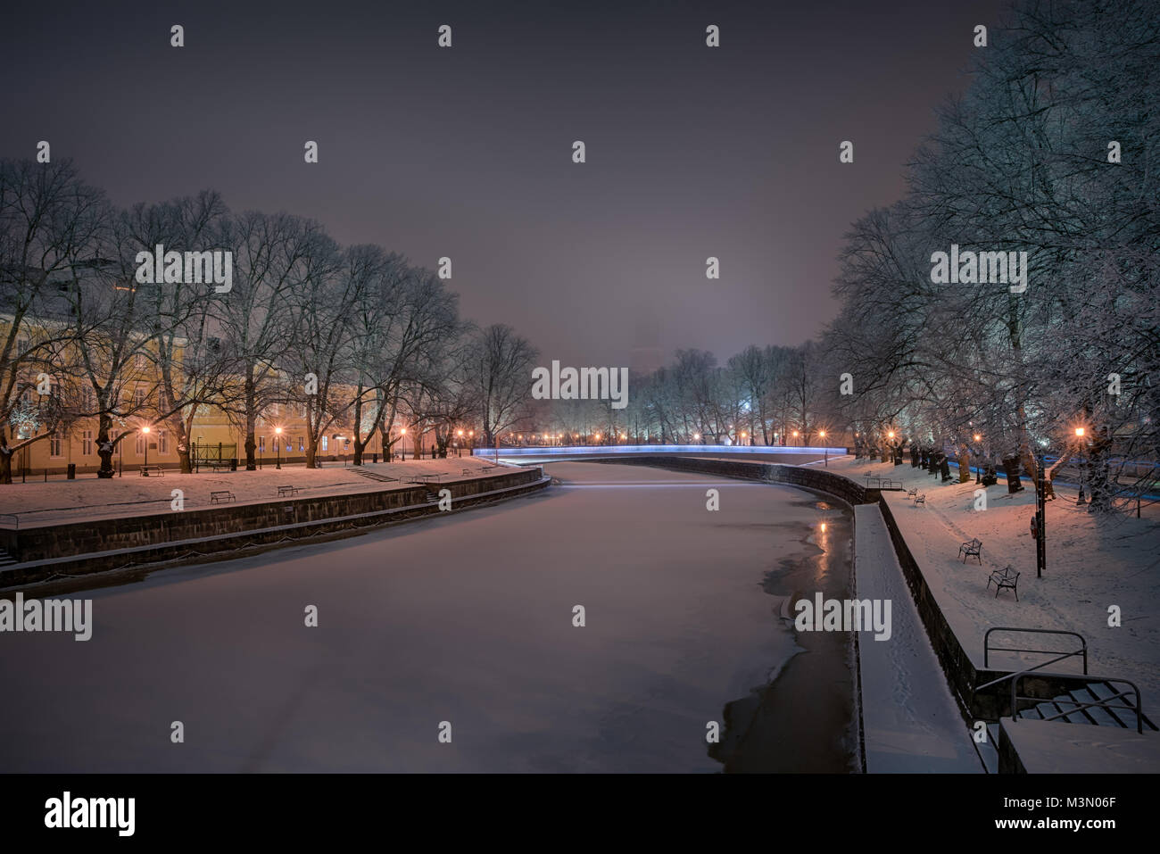 Beautiful view of Aura river with frost covered oak trees on the sides illuminated by streetlight and Turku Cathedral faintly seen in the background i Stock Photo
