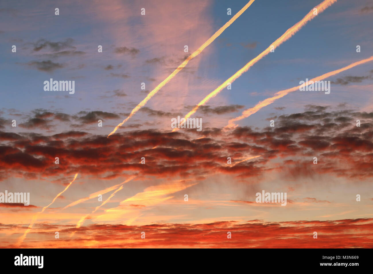 Red morning clouds and streams of condensed vapor on the sky Stock Photo
