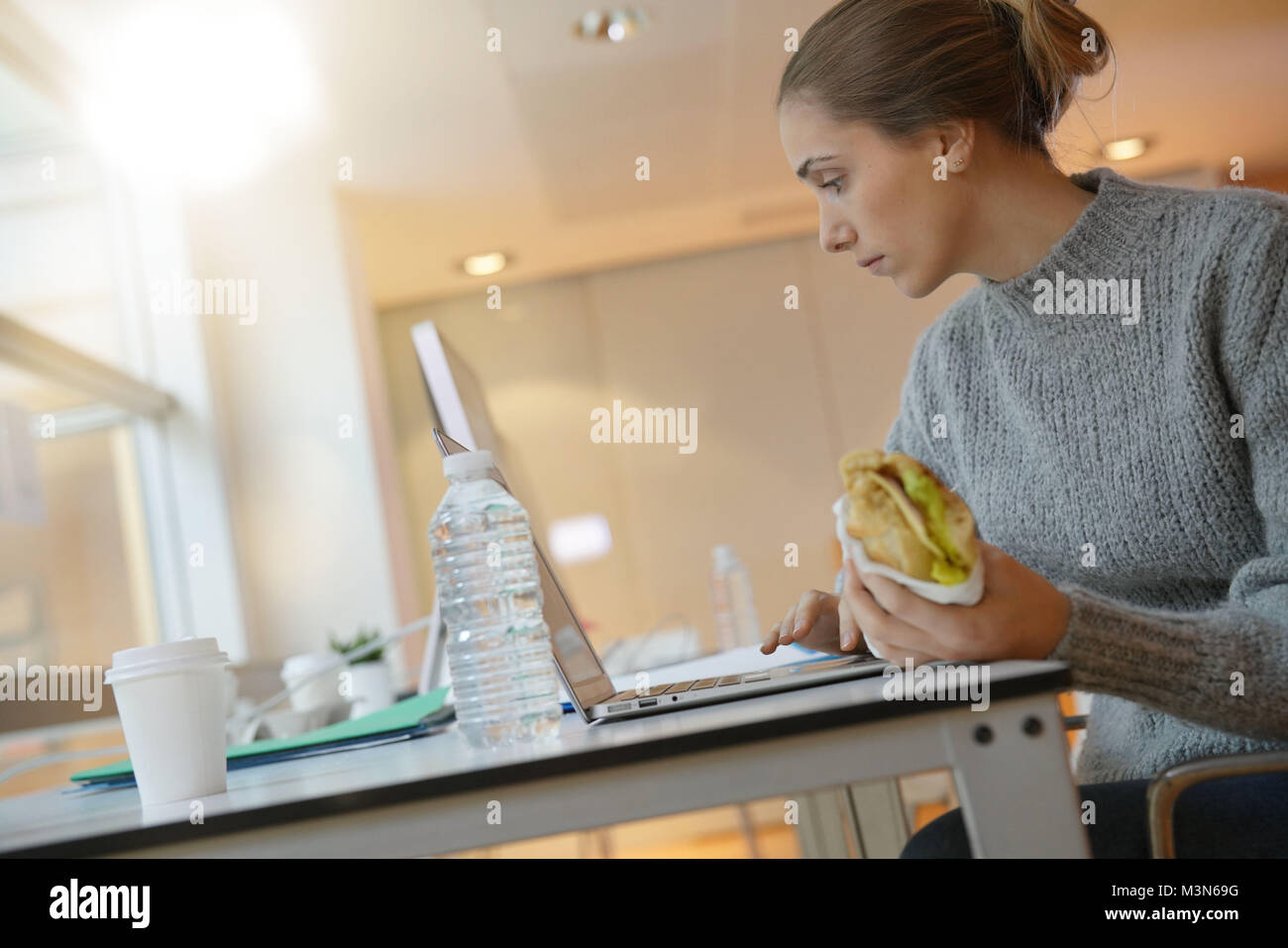 Young woman student eating sandwich in front of laptop computer Stock ...