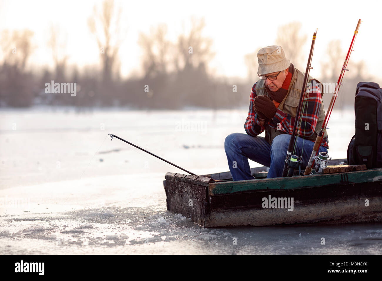 Winter season- elderly man fishing on the frozen river Stock Photo
