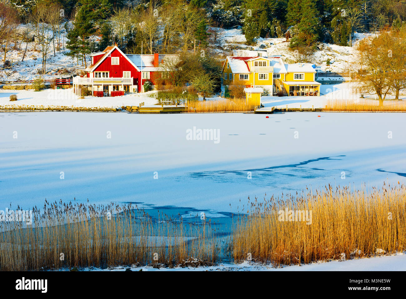 Two seaside homes with private piers in a winter coastal landscape. Bay is fozen and the sun is warming the opposite shore. Bay of Dragsnas outside Ro Stock Photo