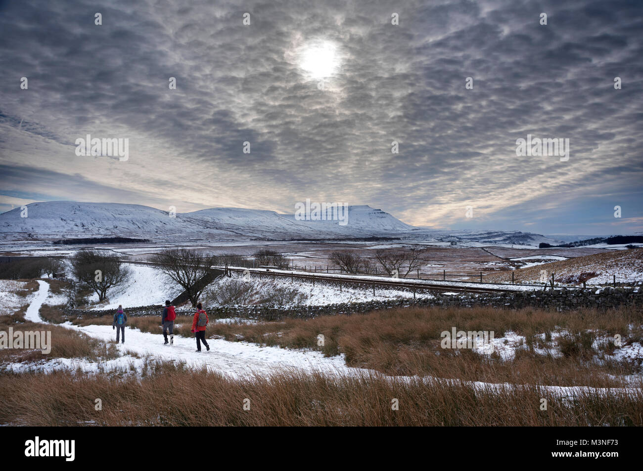 Hazy Winter sun above walkers next to the Settle-Carlisle railway, Ribblehead. Ingleborough peak is on the horizon. Yorkshire Dales National Park, UK. Stock Photo