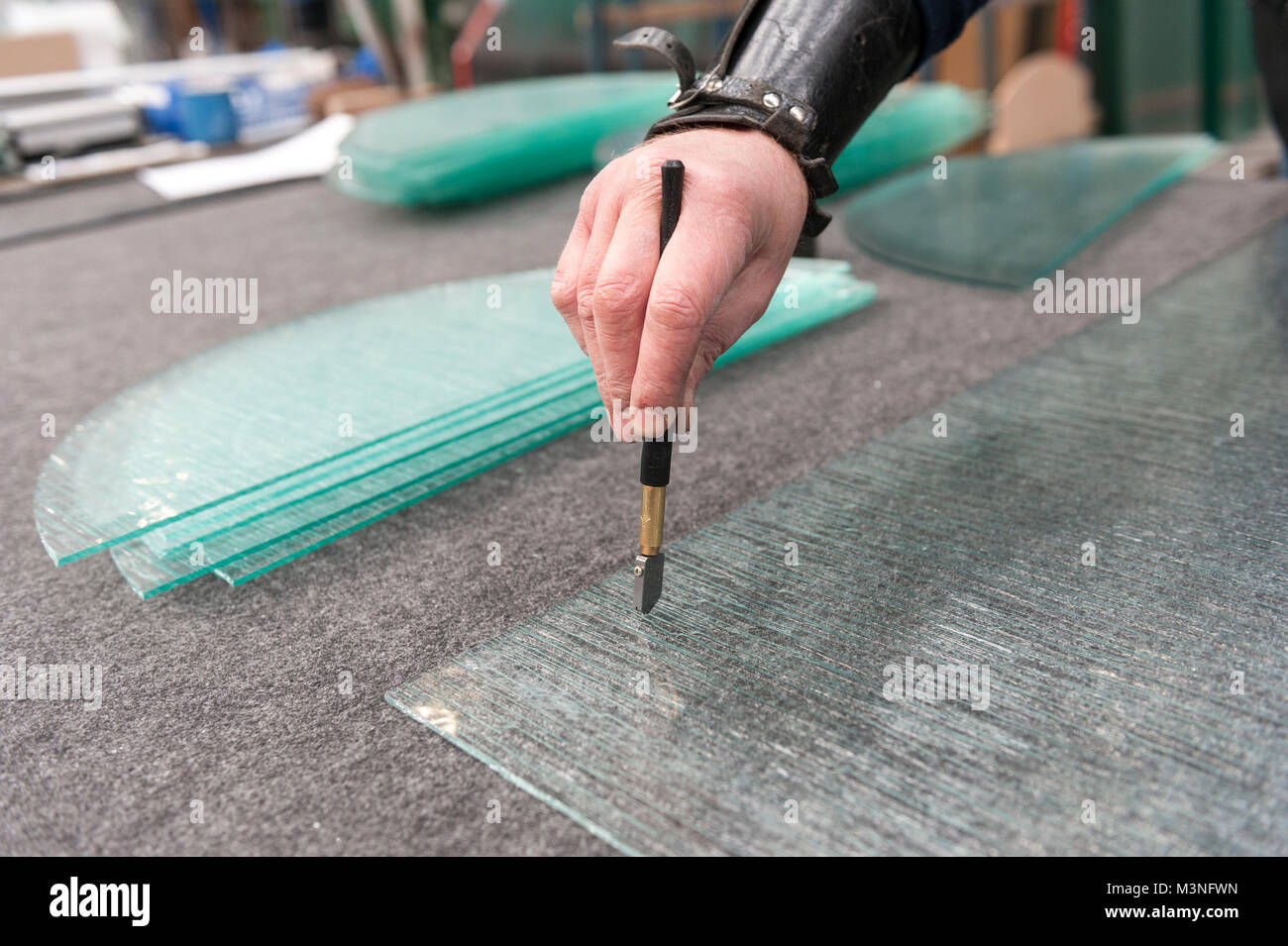 Glass cutting by hand ..A glass cutter tool with diamond blade used to make a shallow score in one surface of a piece of glass that is to be broken in Stock Photo