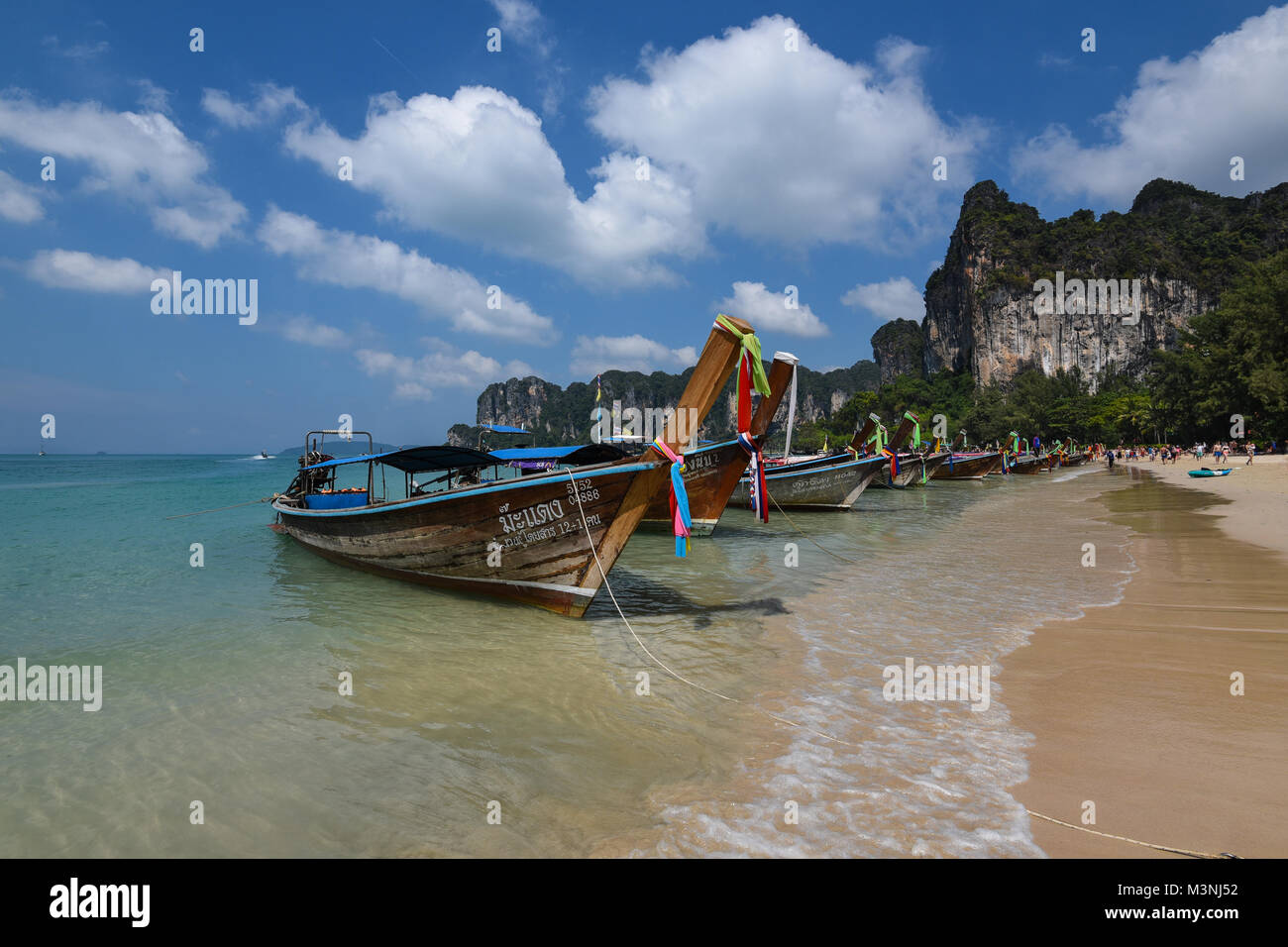 Stunning landscape view of a row of long-tail boats anchored on a beautiful golden sandy beach in Thailand with blue sky and towering cliffs Stock Photo