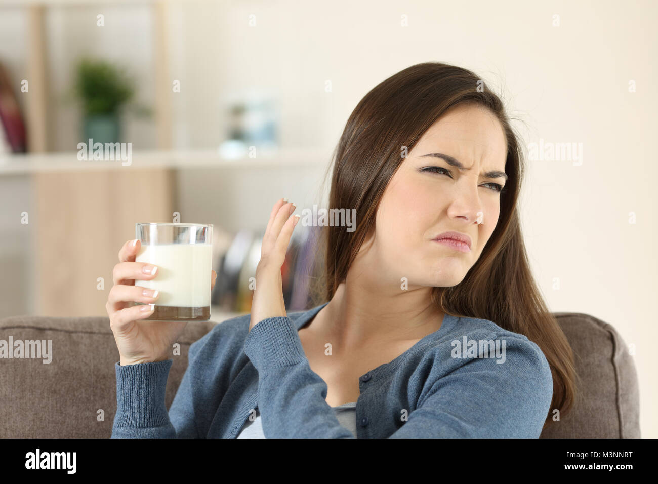 Woman refusing a glass of milk sitting on a couch in the living room at home Stock Photo