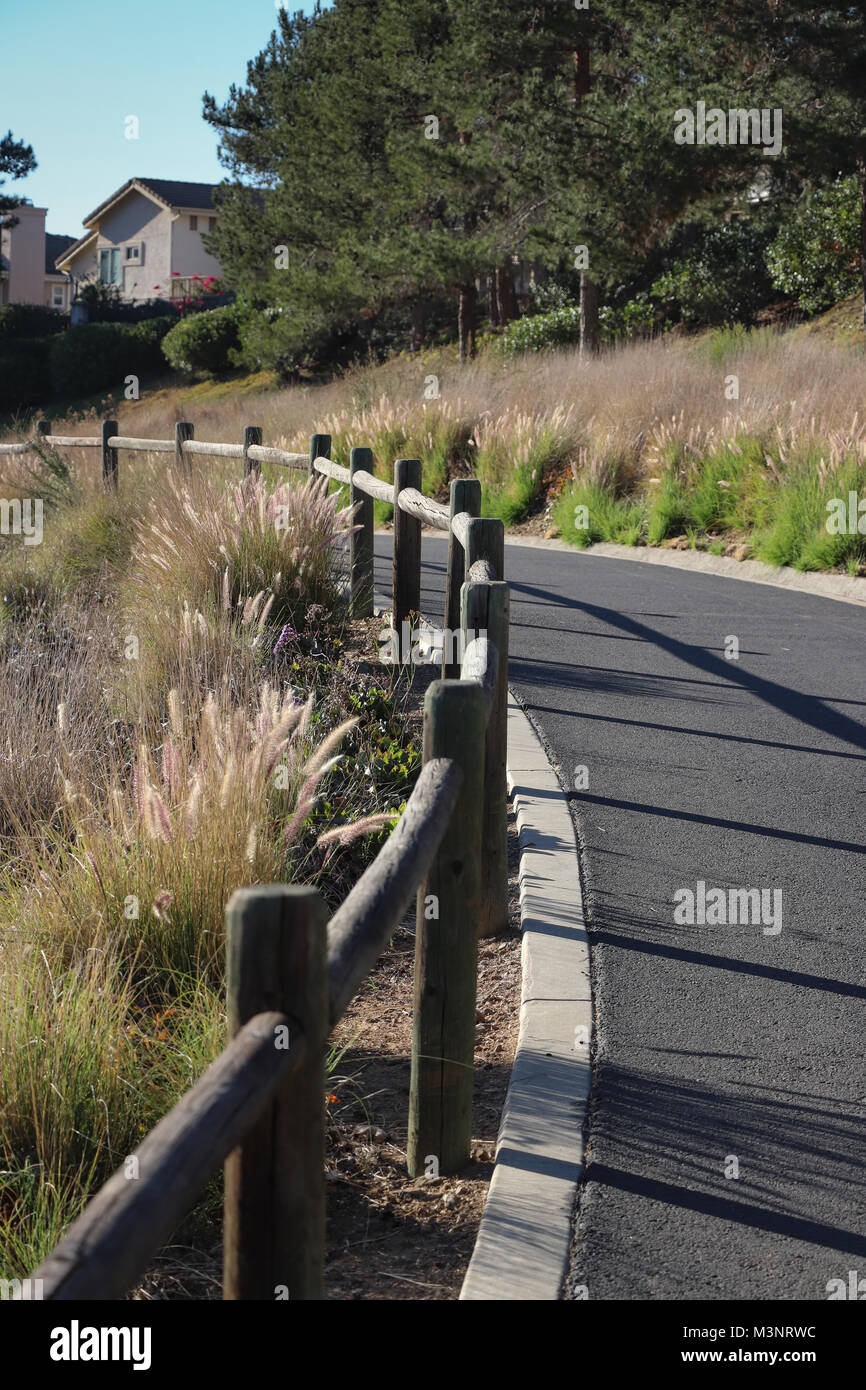 The trail system in San Marcos, CA consists of a paved path with wooden railing, landscaping and concrete curbing that winds through natural areas. Stock Photo