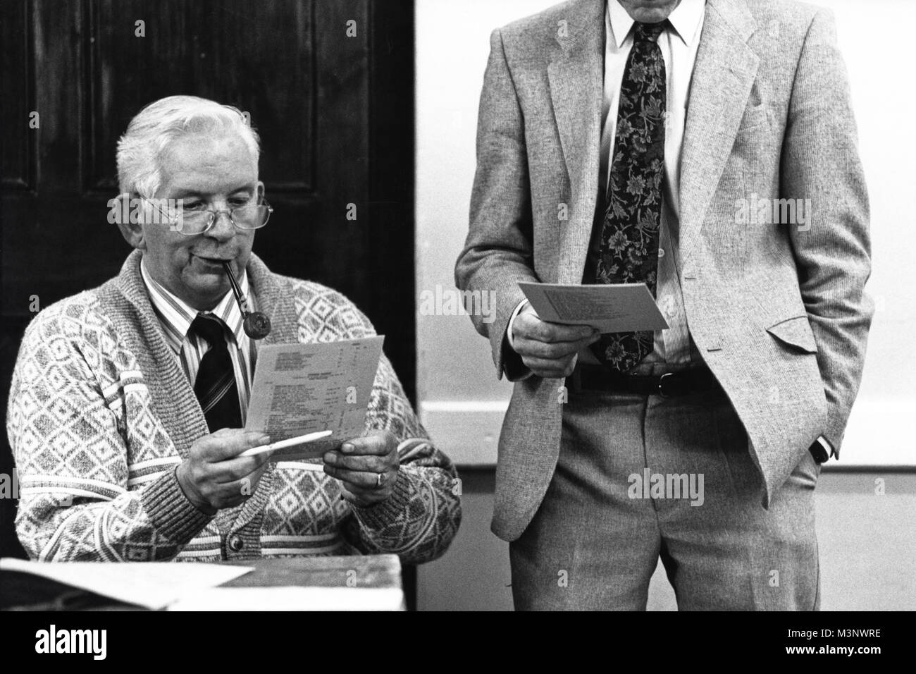 Two men reading programme with one smoking a pipe at small eisteddfod in village hall at Trefeglwys Powys Wales UK Stock Photo
