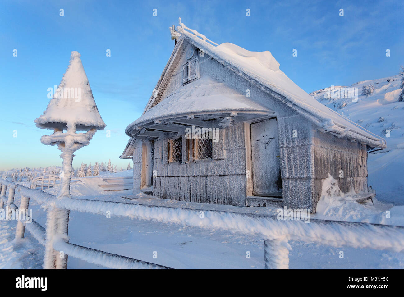 Idyllic frozen old wooden alpine hut covered with snow in the mountain landscape of Velika planina, Slovenia at dusk. Stock Photo