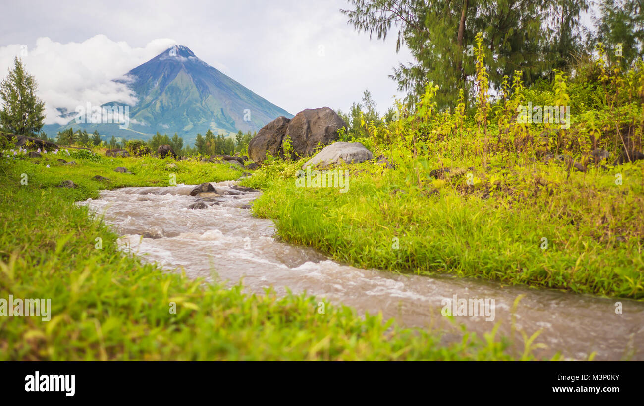 River near Mayon Volcano is an active stratovolcano in the province of Albay in Bicol Region, on the island of Luzon in the Philippines. Renowned as the perfect cone because of its symmetric conical shape. Stock Photo