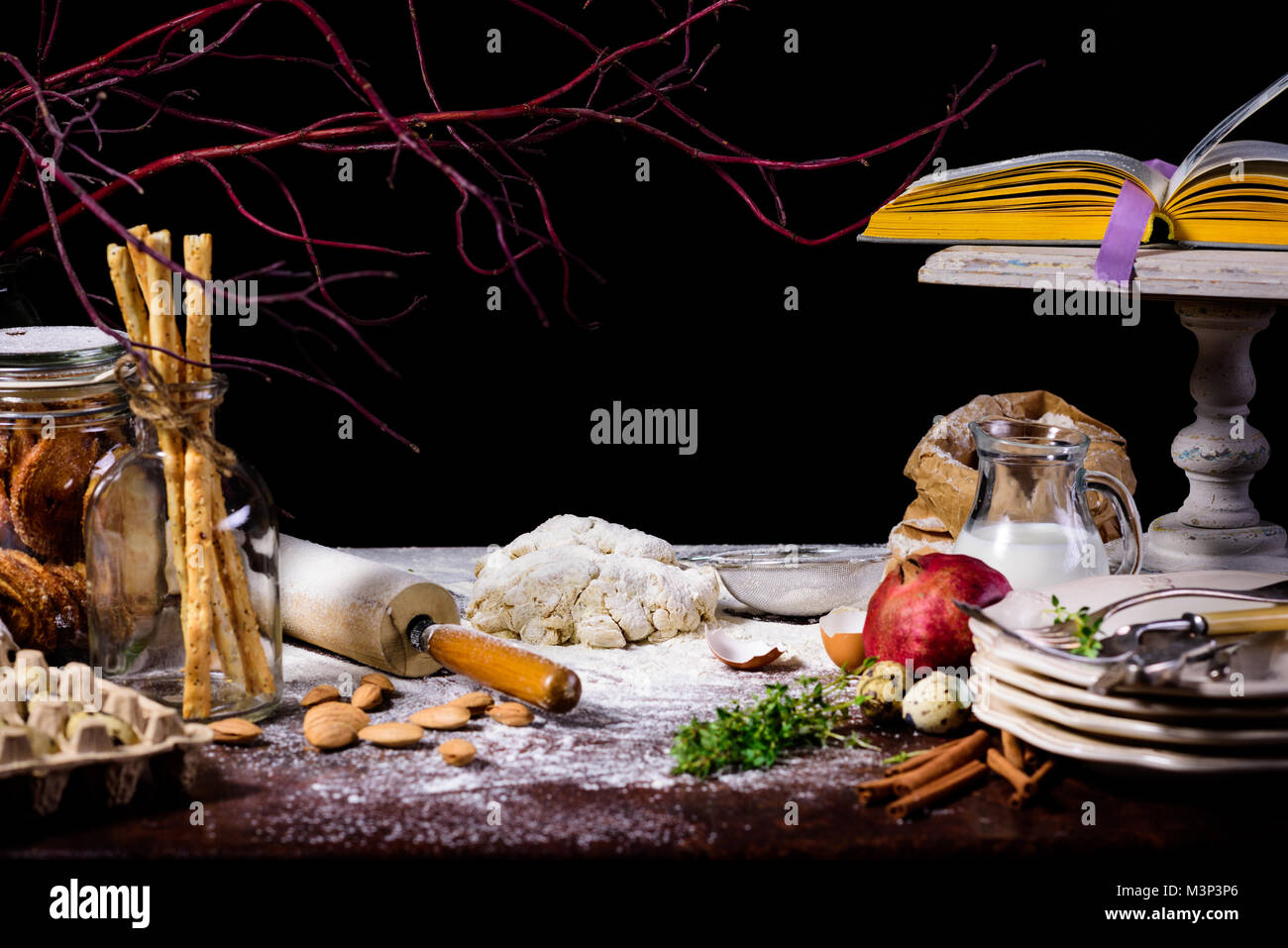 close-up view of dough, rolling pin, dry branch and glass bottle with cookies on black  Stock Photo