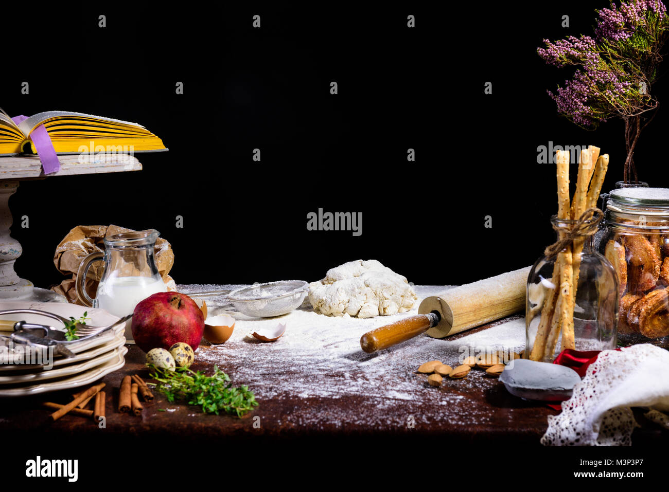 close-up view of dough, rolling pin, dry branch and glass jug with milk on black  Stock Photo