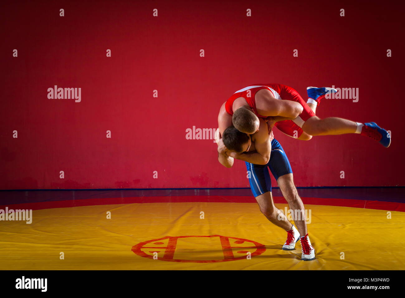 Two greco-roman  wrestlers in red and blue uniform wrestling   on a yellow wrestling carpet in the gym Stock Photo