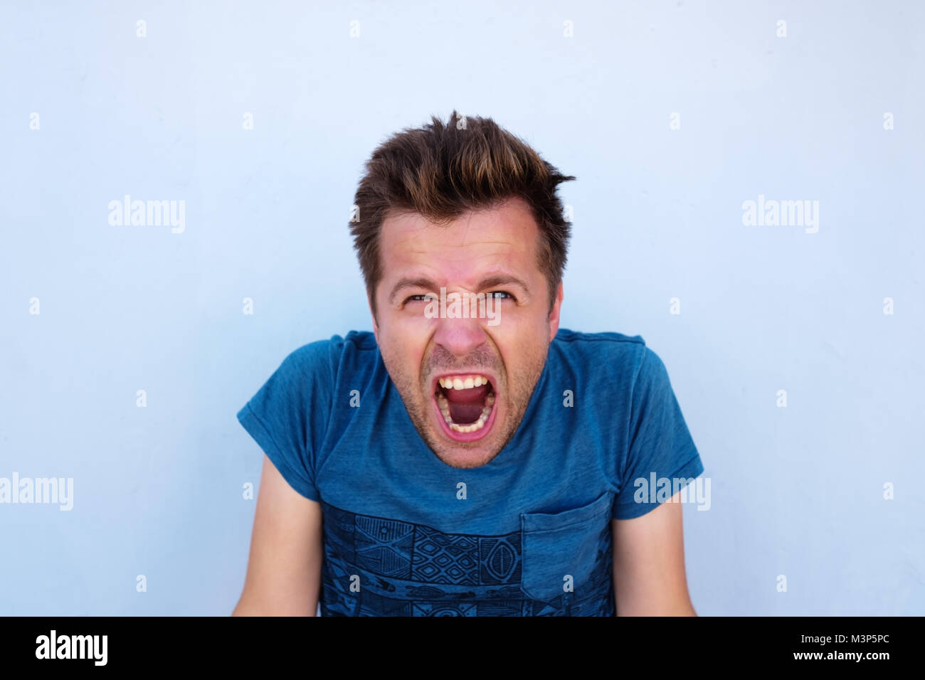 Desperate furious raged man in blue shirt screaming loudly having his eyes full of anger Stock Photo