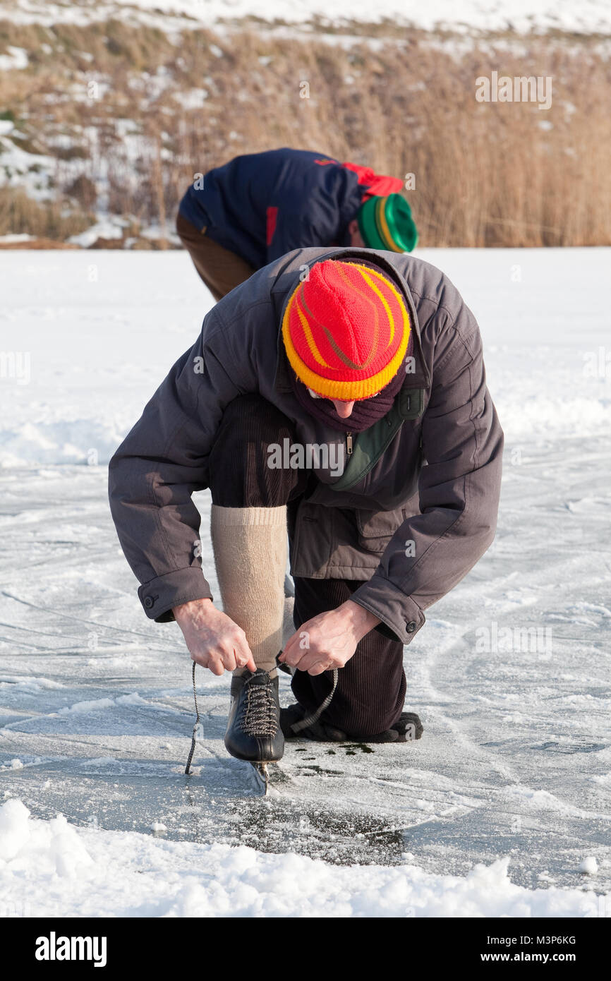 Man fastens the boot of his skate while he is sitting on the ice with one knee Stock Photo