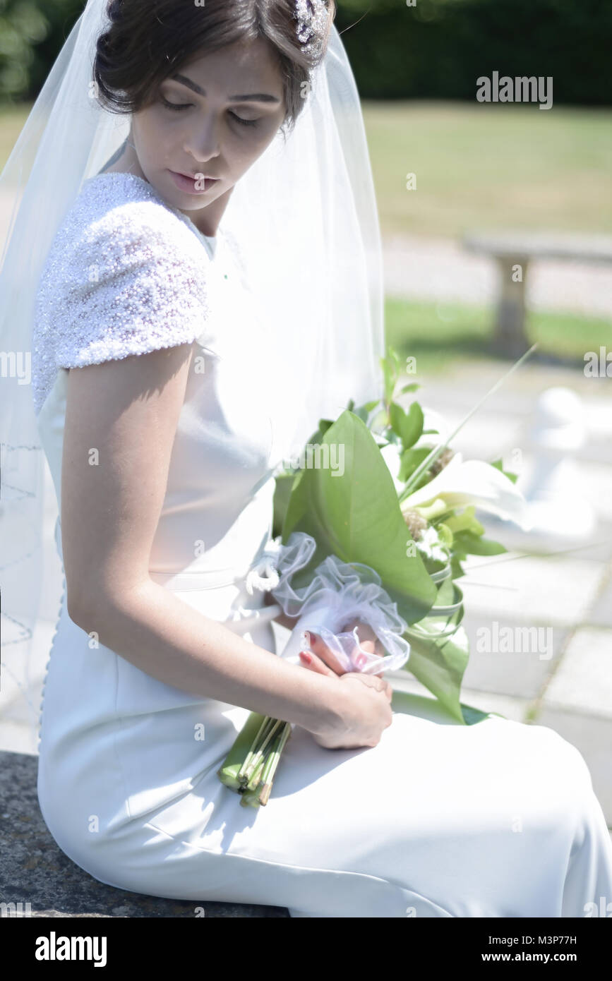 A beautiful dark haired bride wearing a fitted expensive Wedding Dress on a sunny day- brightly lit Stock Photo