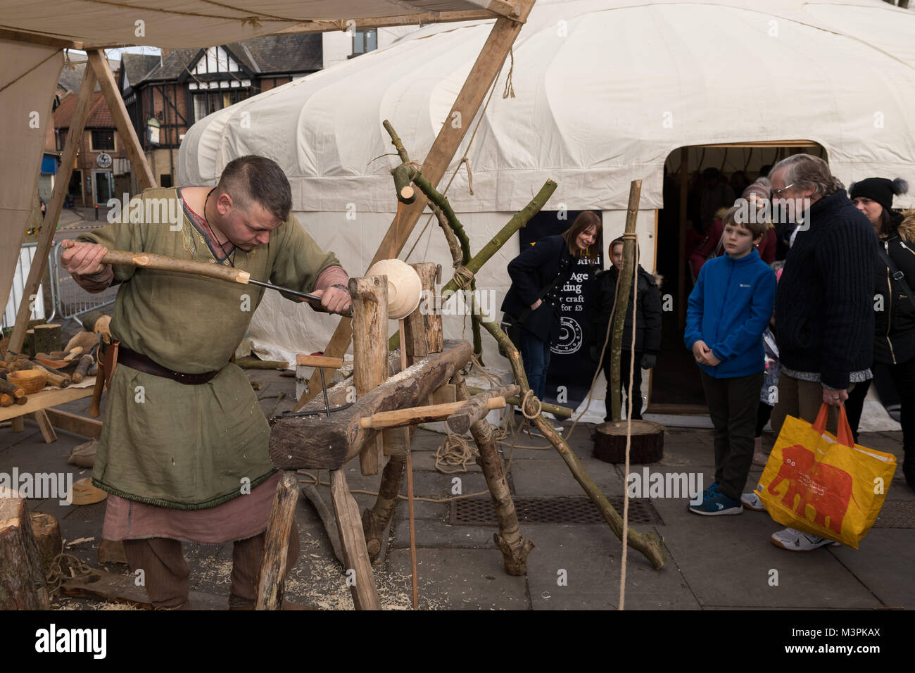York, UK, 12th February 2018. Person dressed as a Viking at the annual Jorvik Viking Festival held in the city centre of York. This man is a skilled wood-turner & is concentrating on crafting a wooden bowl, using a simple lathe & handmade tools. He is taking part in the realistic re-enactment of life at a Viking market & is being watched by members of the public, who are standing close by, fascinated. North Yorkshire, England, UK. Credit: Ian Lamond/Alamy Live News Stock Photo