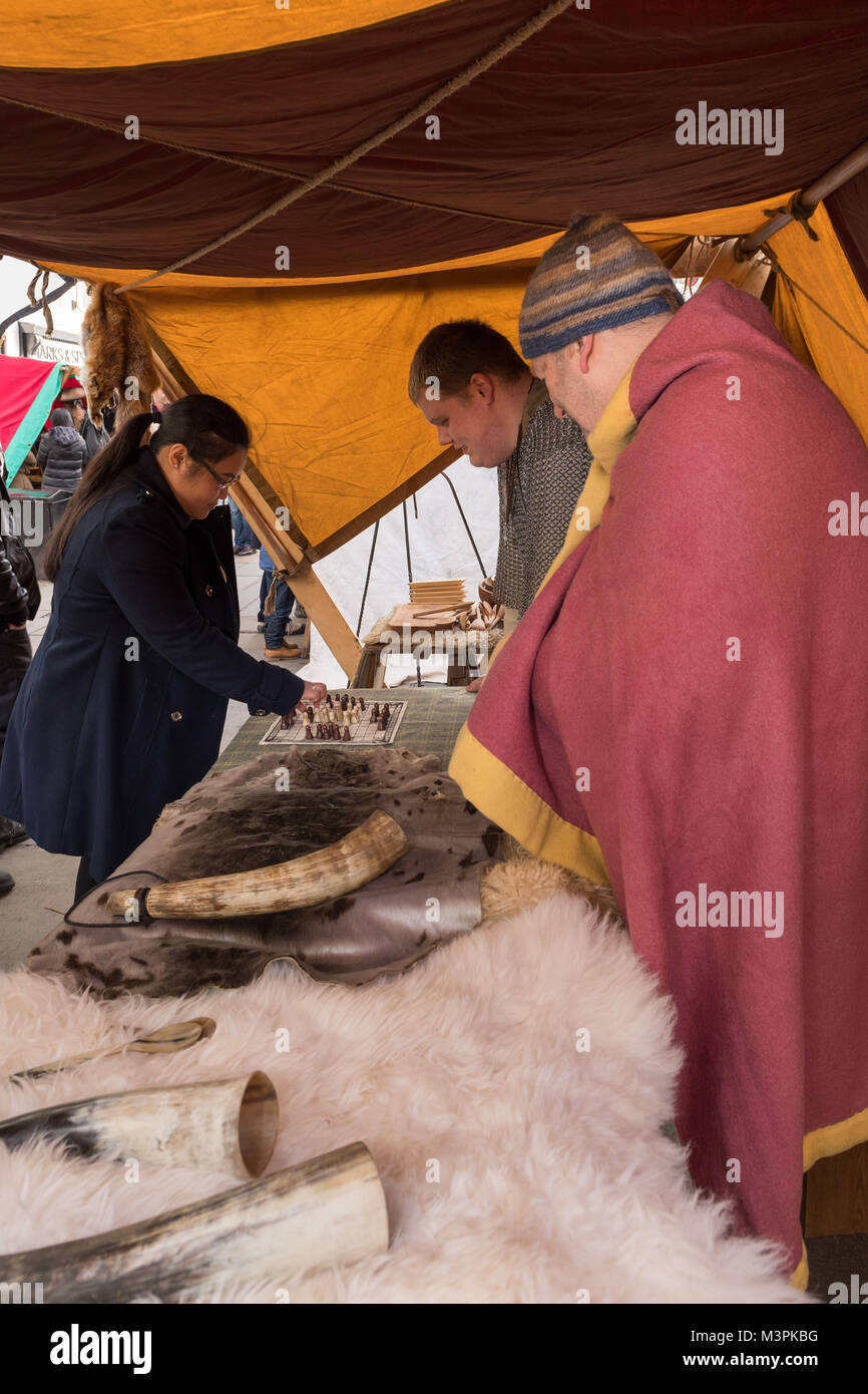 York, UK, 12th February 2018, People dressed as Vikings at the annual Jorvik Viking Festival. A female member of the public is playing a game of hnefatafl with one of the men. Items on their stall are made from animal skin and bone or antler. Both are taking part in a realistic re-enactment of life at a Viking market. City centre of York, North Yorkshire, England, UK.  Credit: Ian Lamond/Alamy Live News Stock Photo