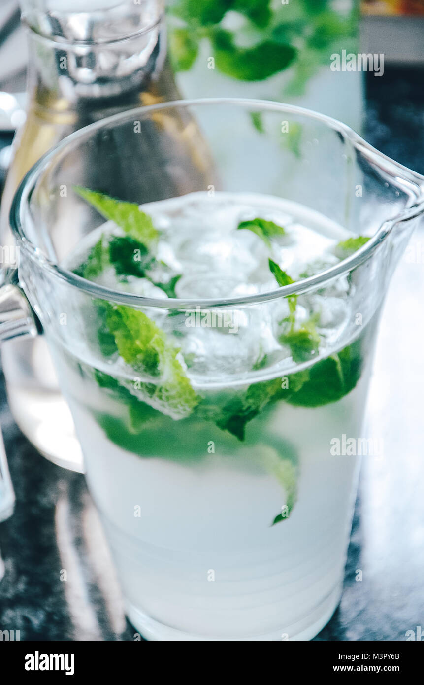 Glass jug with cold water infused with peppermint leaves to make a
