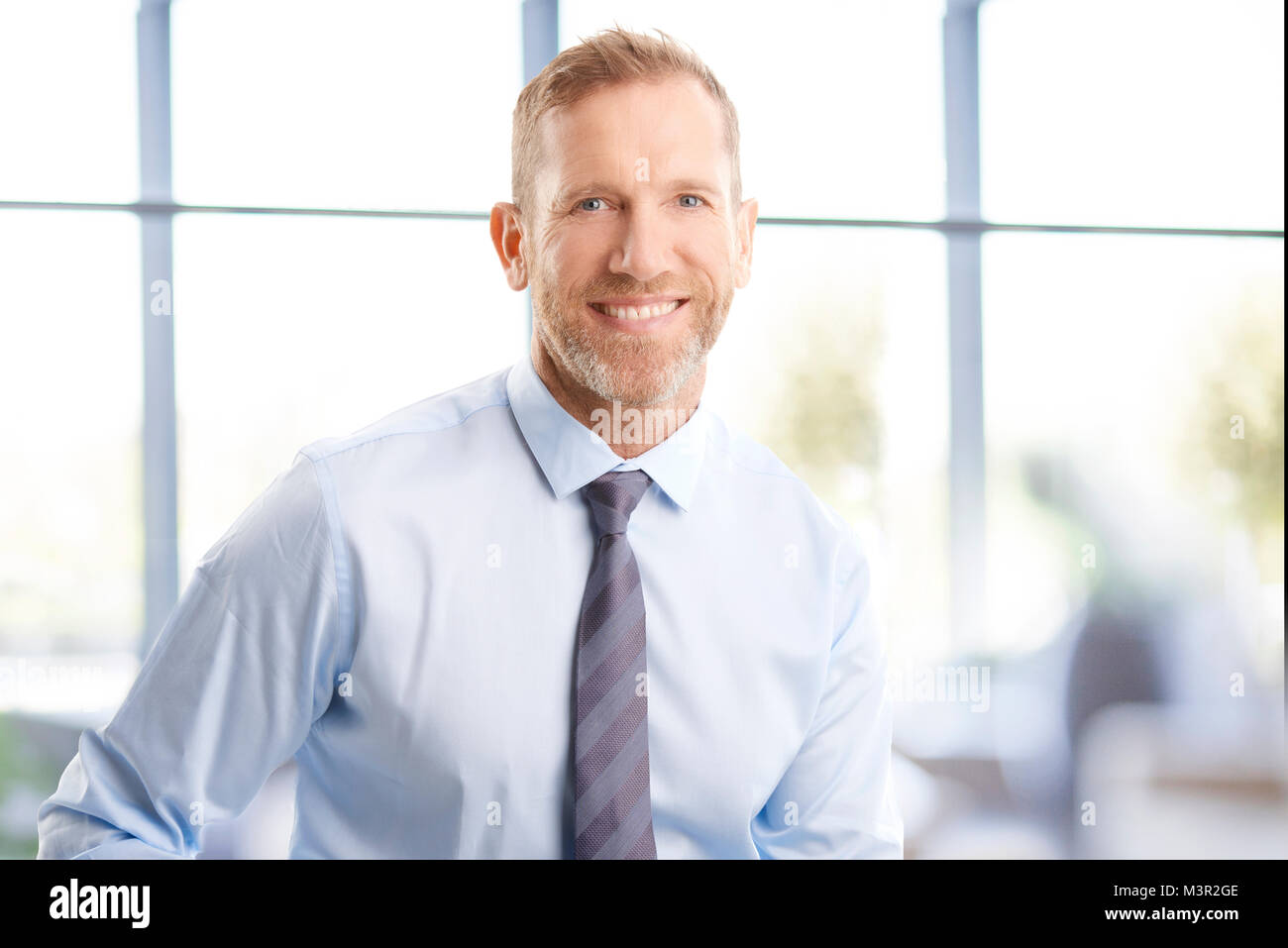 Portrait of businessman with toothy smile standing at the officde and ...