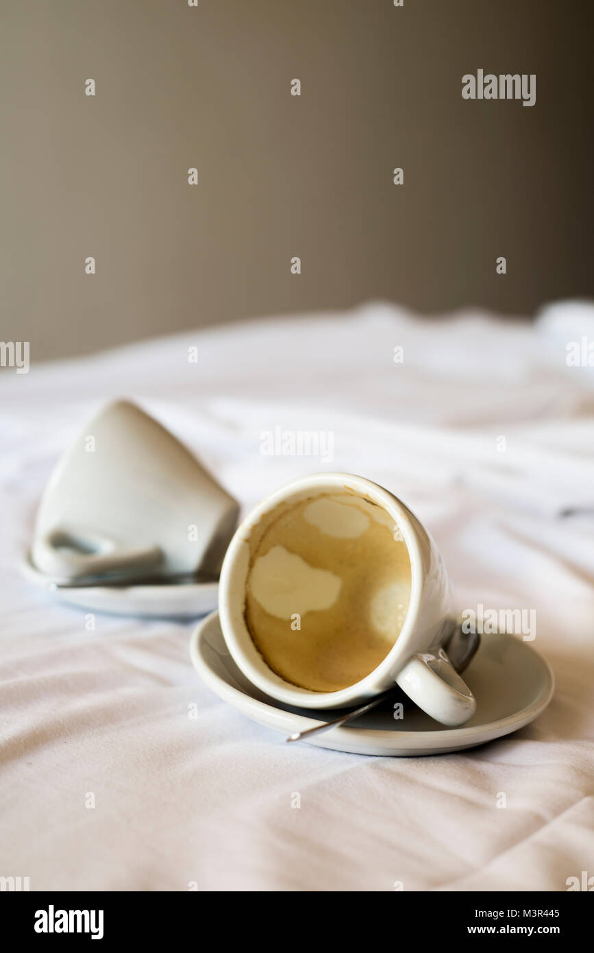 two white ceramic empty cups of coffee on the white sheets of an unmade bed Stock Photo