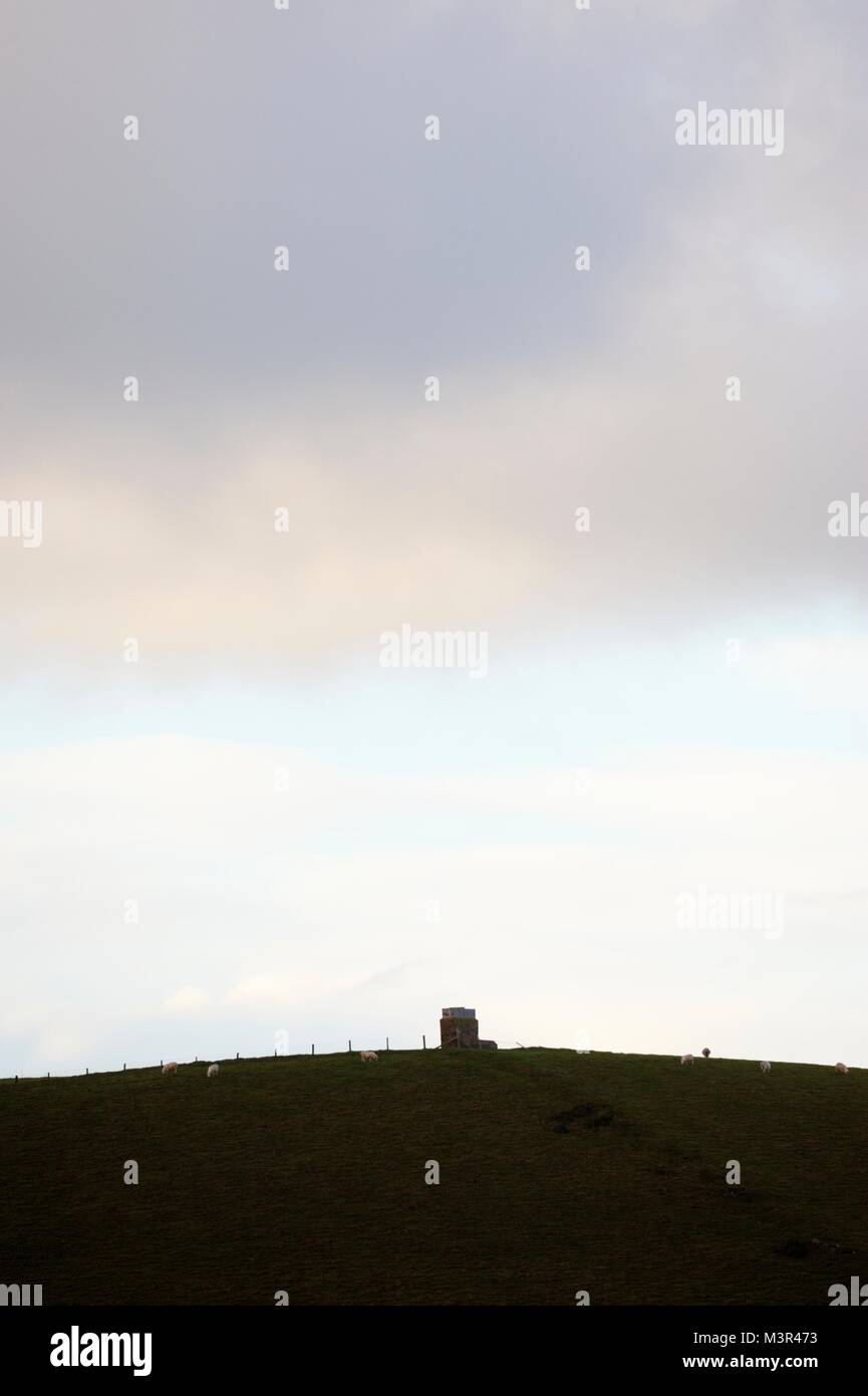 Square stone structure on a curved hilltop with sheep grazing, Wales, UK. Stock Photo
