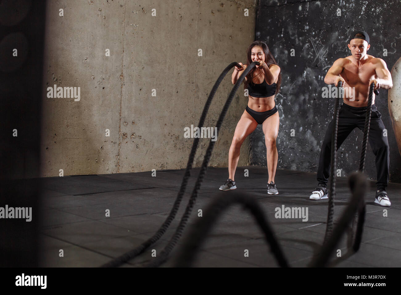Woman and man couple training together doing battling rope workout ...