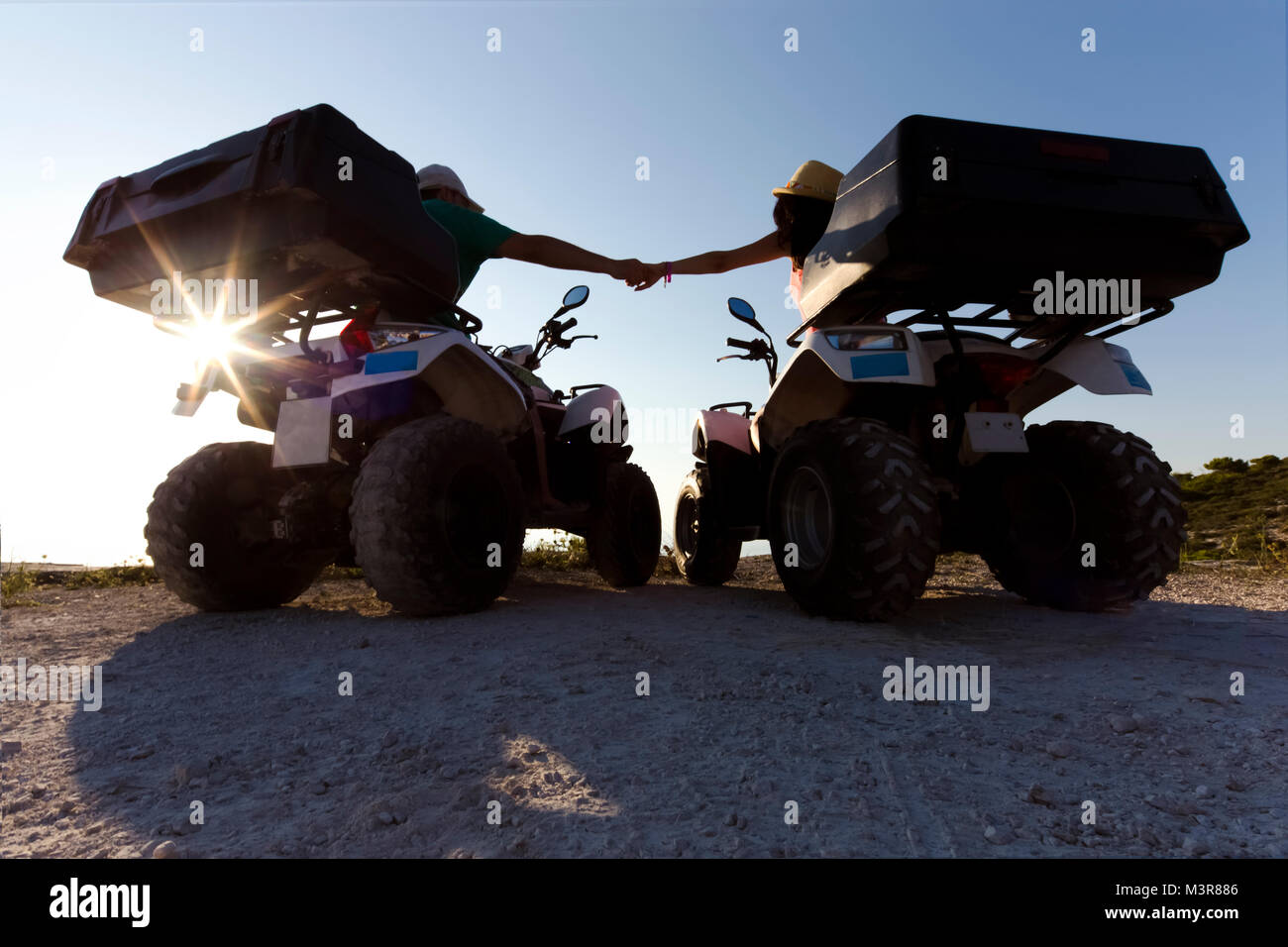 couple in love on quad bikes holding hands watching the sunset, silhouette photo, rear view, Zakynthos Stock Photo