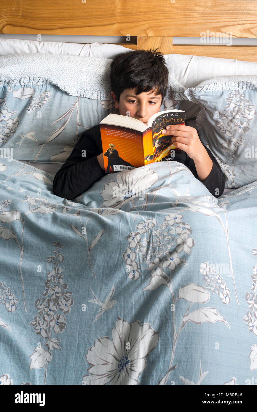Boy reading  book in bed ,Harry Potter by J.K.Rowling ,UK Stock Photo