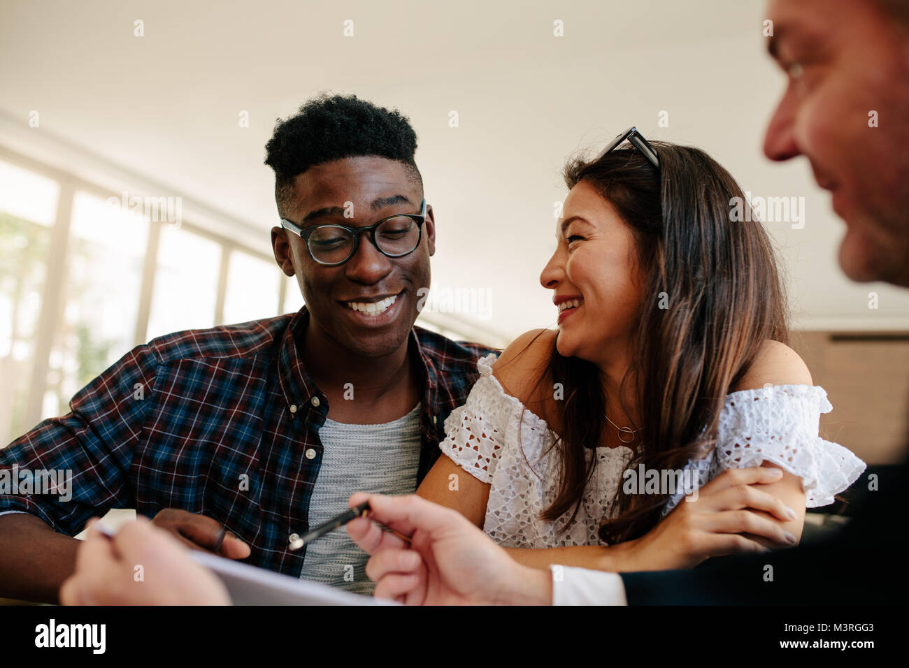 Happy interracial couple looking at their new house lease agreement and smiling with estate broker. Young couple renting a new house. Stock Photo