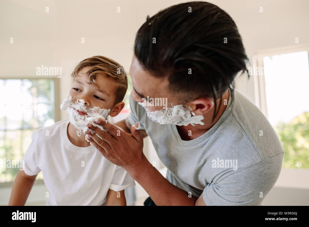 Man applying shaving foam in his sons face in bathroom. Father and son shaving together in