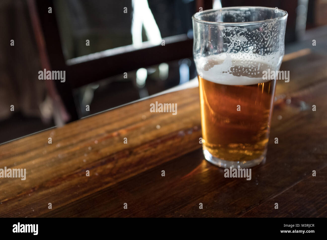 Half full pint of beer on pub table Stock Photo