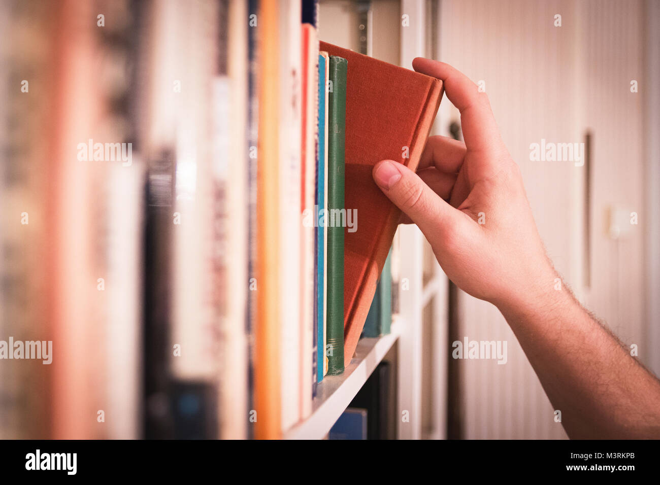 Hand reaching for classic book in library. Stock Photo