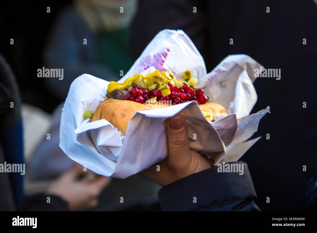 Hand holding a hot dog with toppings (lingonberry and pickle) at the Scandinavian Christmas Market, London, UK Stock Photo
