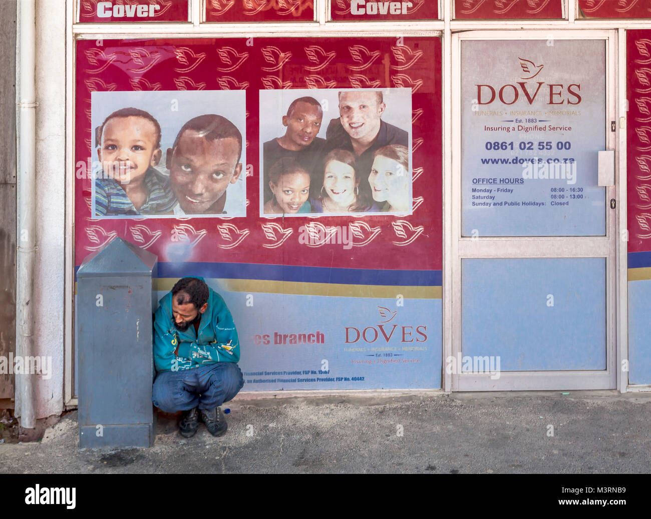Street scene in Cape Town, South Africa. The man is crouching in front of a business that offers funeral services. Stock Photo